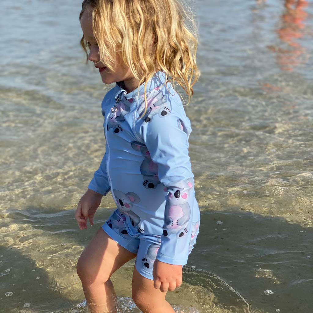 Girl At Beach Walking In Shallow Water While Wearing Blue Koala Unisex Zip Swimmers