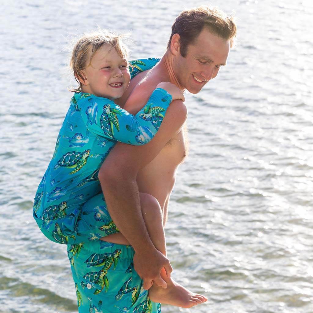 Boy Wearing Blue Turtle Kids' Boardshorts While Being Carried on Back Of Man