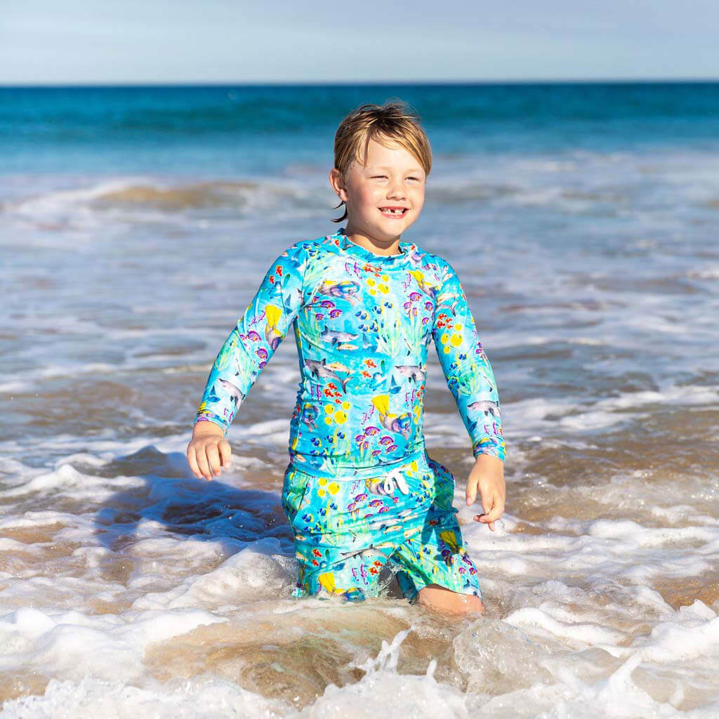 Smiling Boy Wearing Great Barrier Reef Kids' Boardshorts At Beach