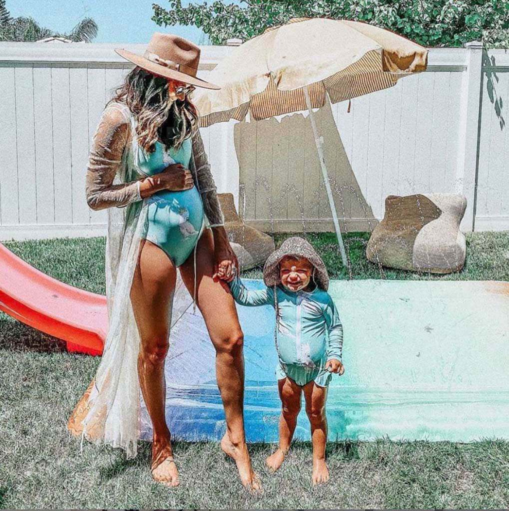 Woman With Toddler Standing Under Sprinkler While Wearing Green Cockatoo Women's One Piece Swimmers
