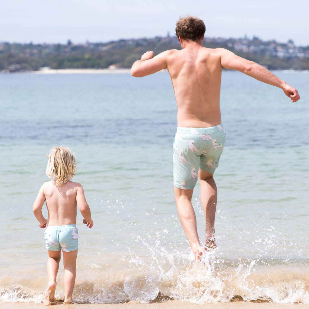 Man Jumping It Water at Beach While Wearing Green Cockatoo Men's Boardshorts