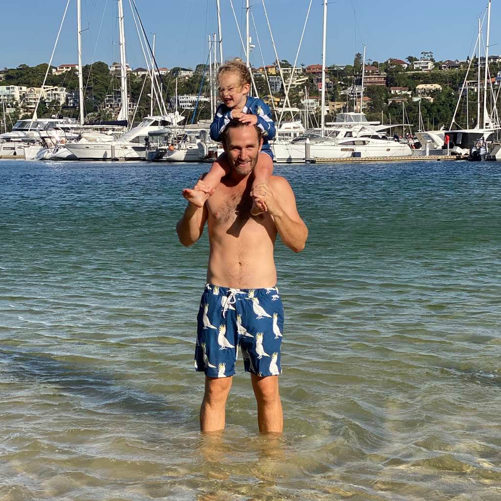 Dad With Child On Shoulders At Beach. Dad Wearing Navy Cockatoo Men's Boardshorts