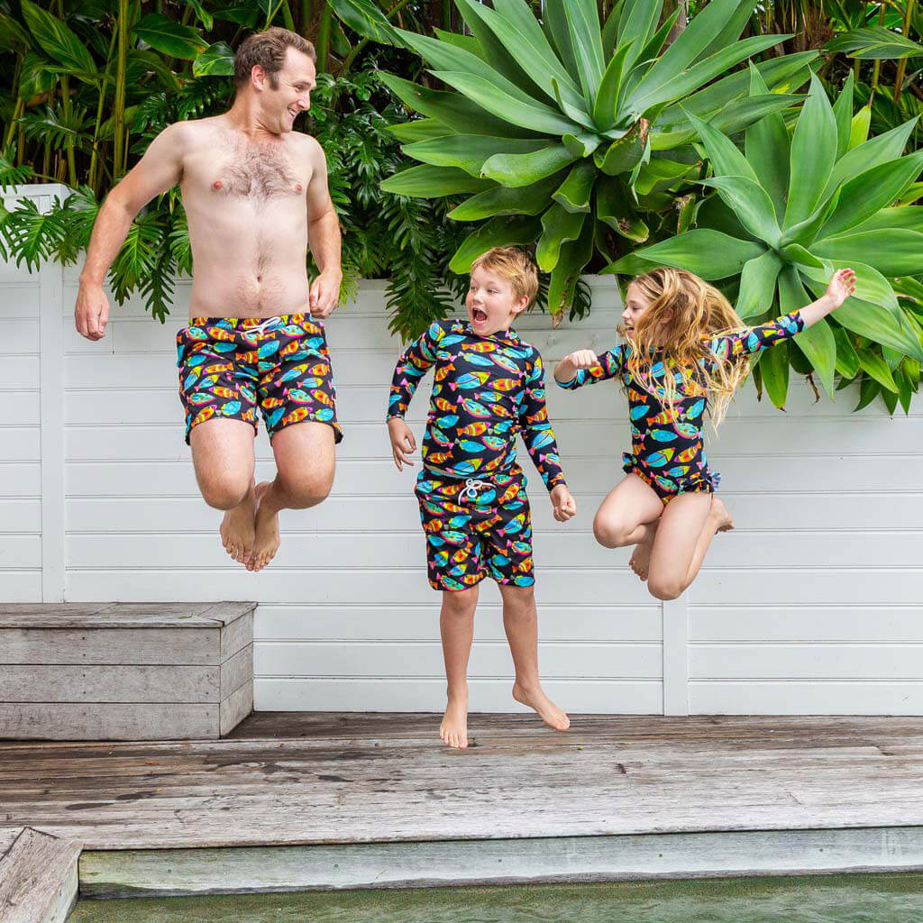 Boy Jumping With Dad and Sister While Wearing Neon Fish Kids' Boardshorts